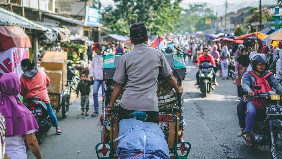 Photo from behind of man on bicycle in busy street in Bandung City, Indonesia. 